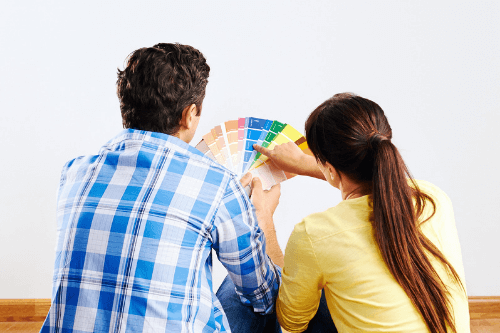 5 Summer Paint Trends For 2021 with Northshore Renovations in Madisonville, La. image of couple sitting on wooden floor facing a white wall with fanned out paint samples to choose from