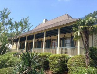 custom painting with Northshore Renovations and Contracting in St. Tammany Parish, LA image of outside of residential home with custom paint job in yellow and evergreen shutters and accents with southern palm landscaping around front porch