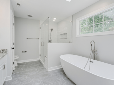 bathroom remodel, home renovations in Madisonville, LA at Northshore Renovations and Contracting. Modern bathroom featuring a freestanding white bathtub, walk-in glass shower with handheld showerhead, large vanity with granite countertop, and gray tile flooring.