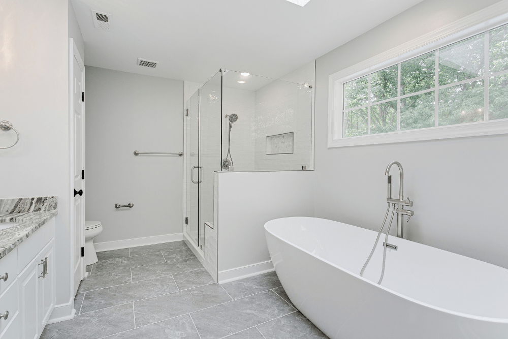 bathroom remodel, home renovations in Madisonville, LA at Northshore Renovations and Contracting. Modern bathroom featuring a freestanding white bathtub, walk-in glass shower with handheld showerhead, large vanity with granite countertop, and gray tile flooring.